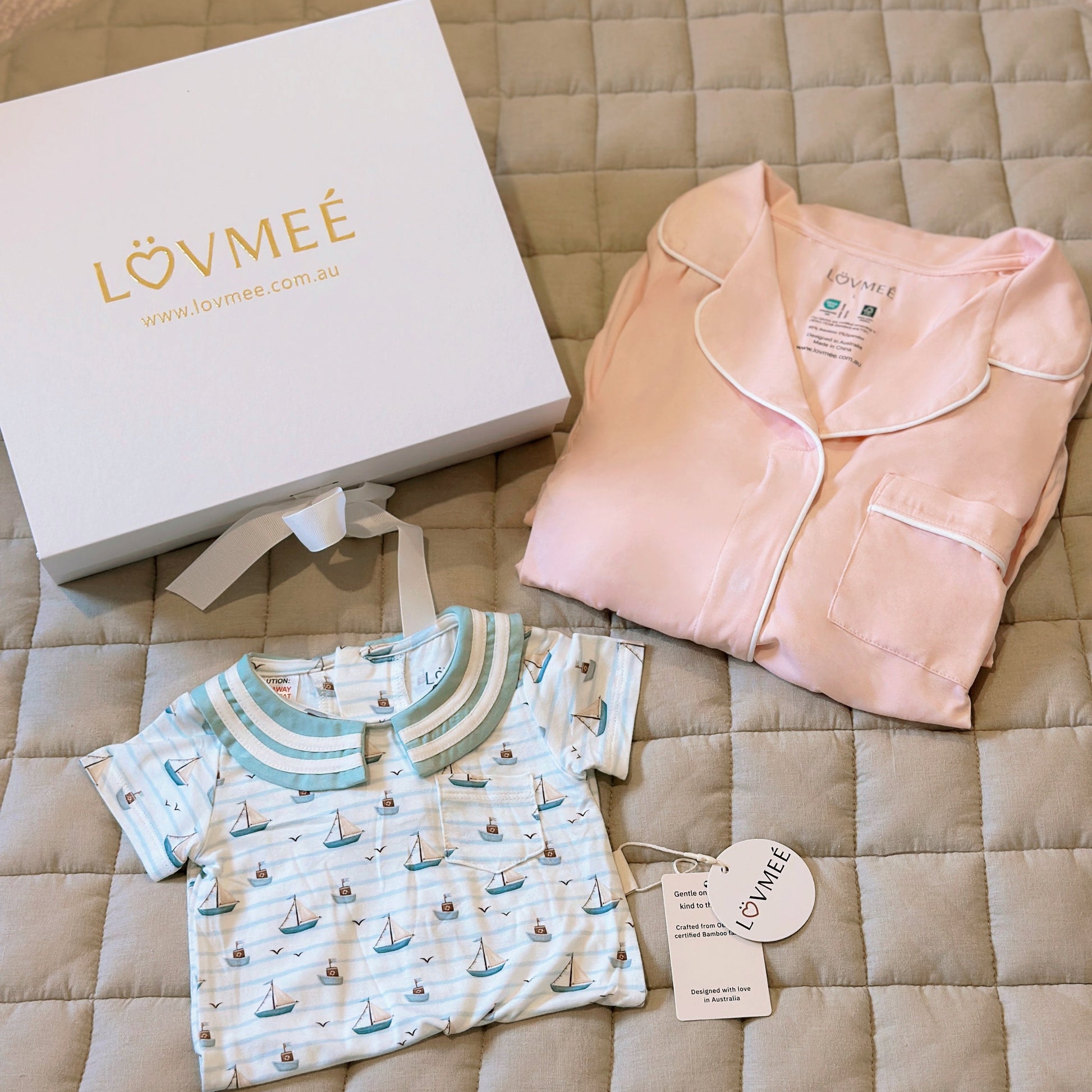 Baby clothing set with pink outfit and sailboat-patterned shirt on a quilted surface, featuring Lövmeé branding.