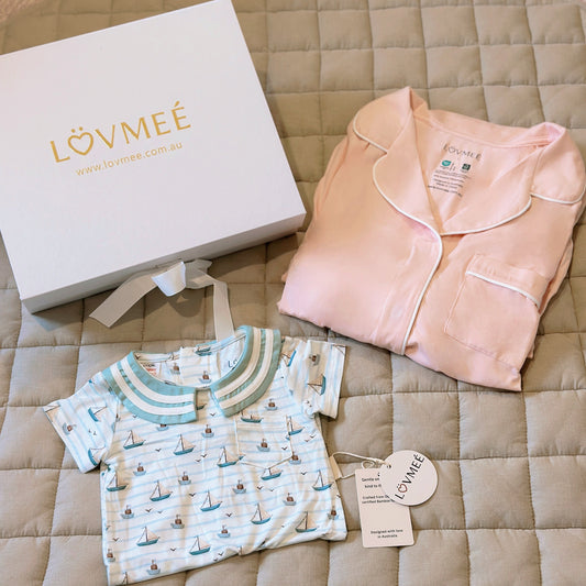 Baby clothing set with pink outfit and sailboat-patterned shirt on a quilted surface, featuring Lövmeé branding.