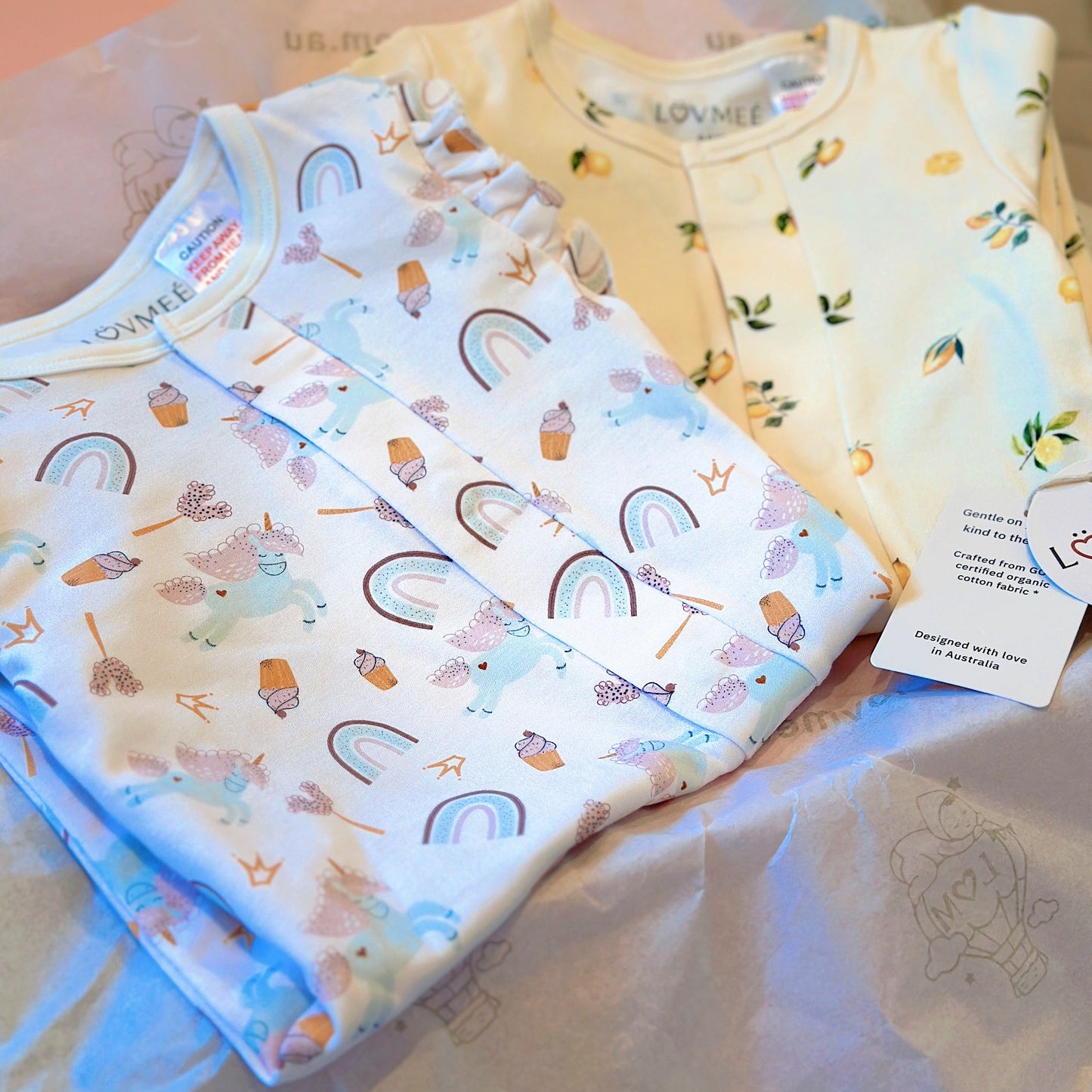 Three baby onesies with colorful patterns on a light pink surface