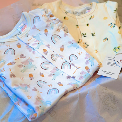 Three baby onesies with colorful patterns on a light pink surface